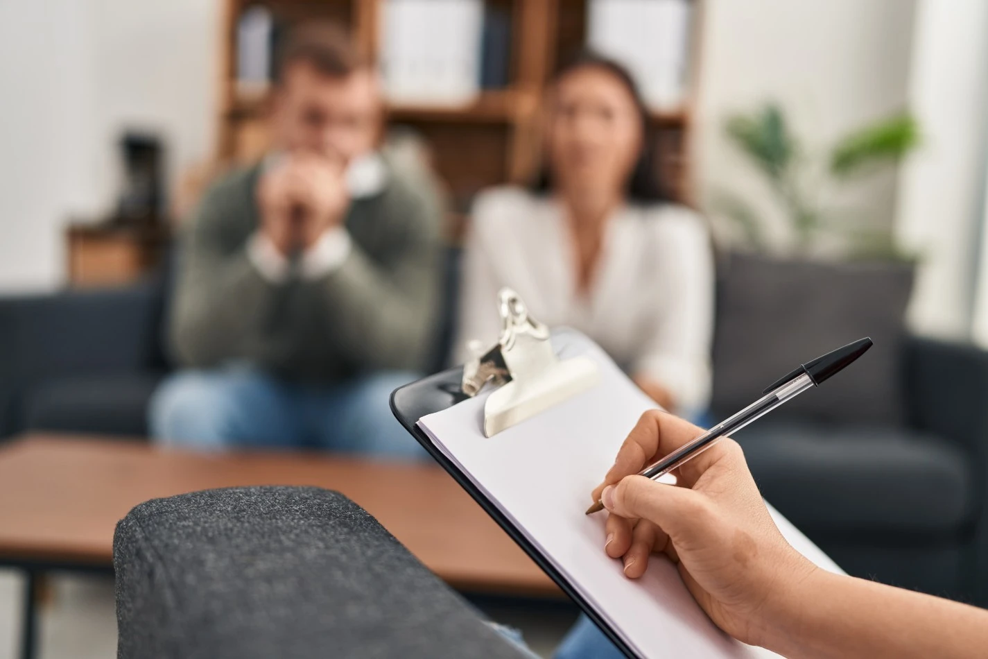 Close up of counsellor writing on clipboard with couple blurred out in the background